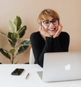 Cheerful woman smiling while sitting at table with laptop